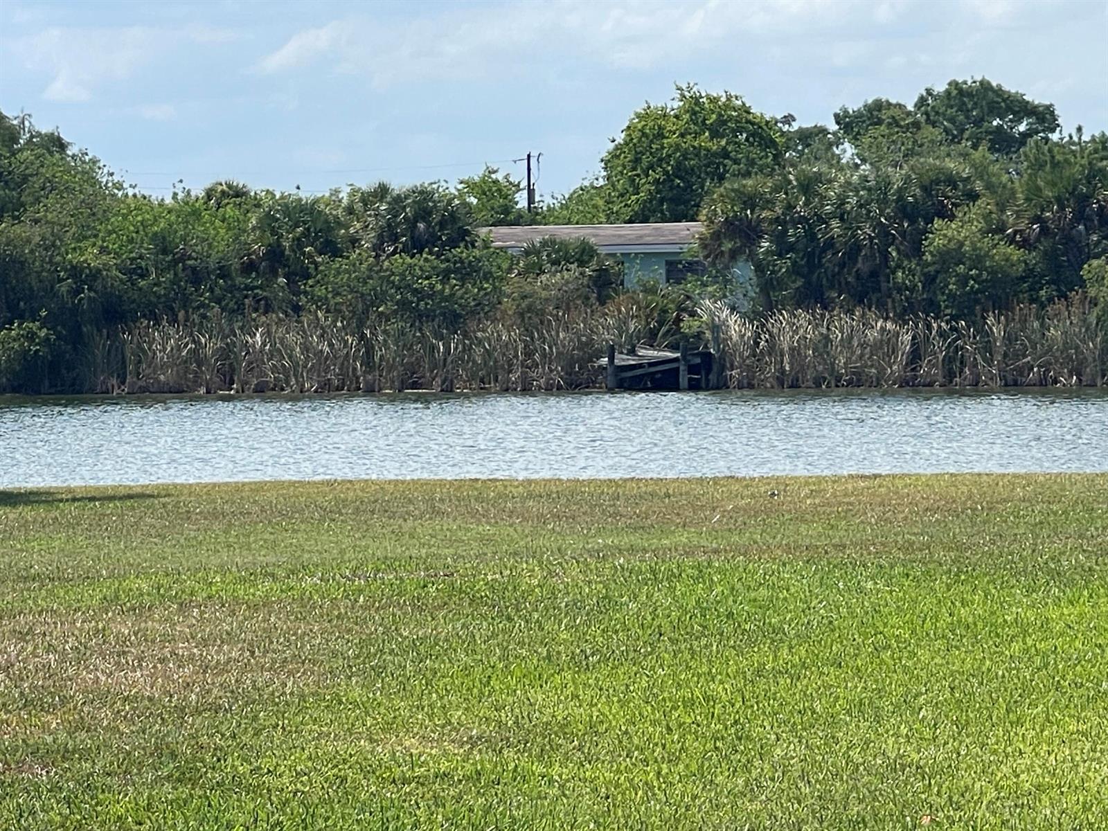 A grassy lawn overlooks a pond with a small wooden dock and dense vegetation — 265 State Rd 78, Moore Haven FL 33471, MOORE HAVEN, FL