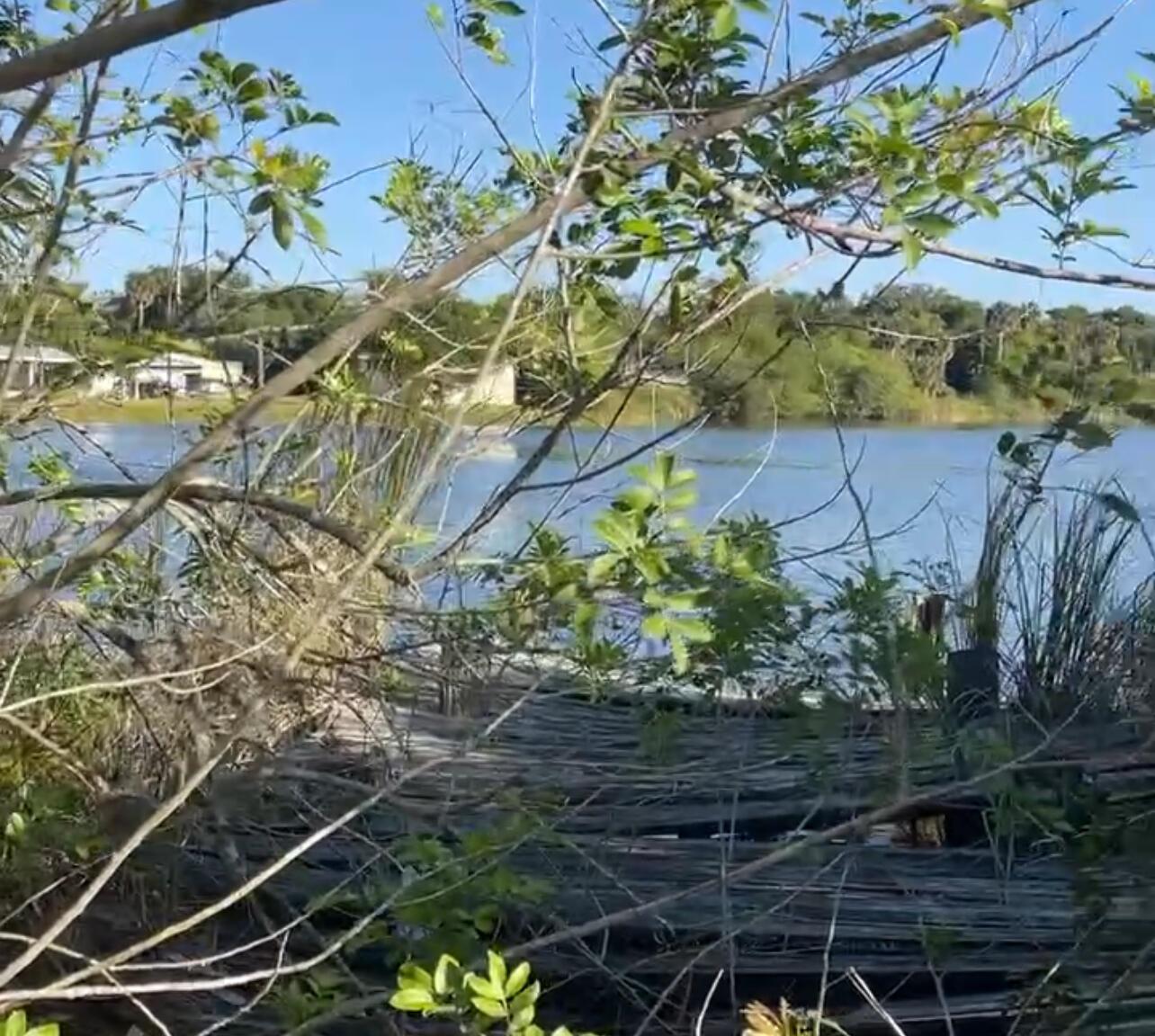 A view of a lake framed by tree branches with a wooden dock in the foreground — 265 State Rd 78, Moore Haven FL 33471, MOORE HAVEN, FL