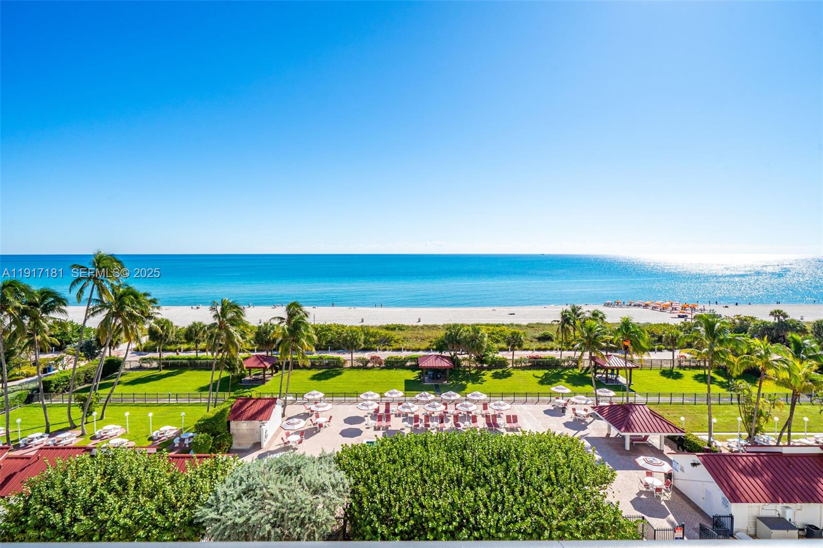 An elevated view shows a beach, ocean, palm trees, and a patio with umbrellas — 2555 Collins Ave # 805, Miami Beach FL 33140, MIAMI BEACH, FL