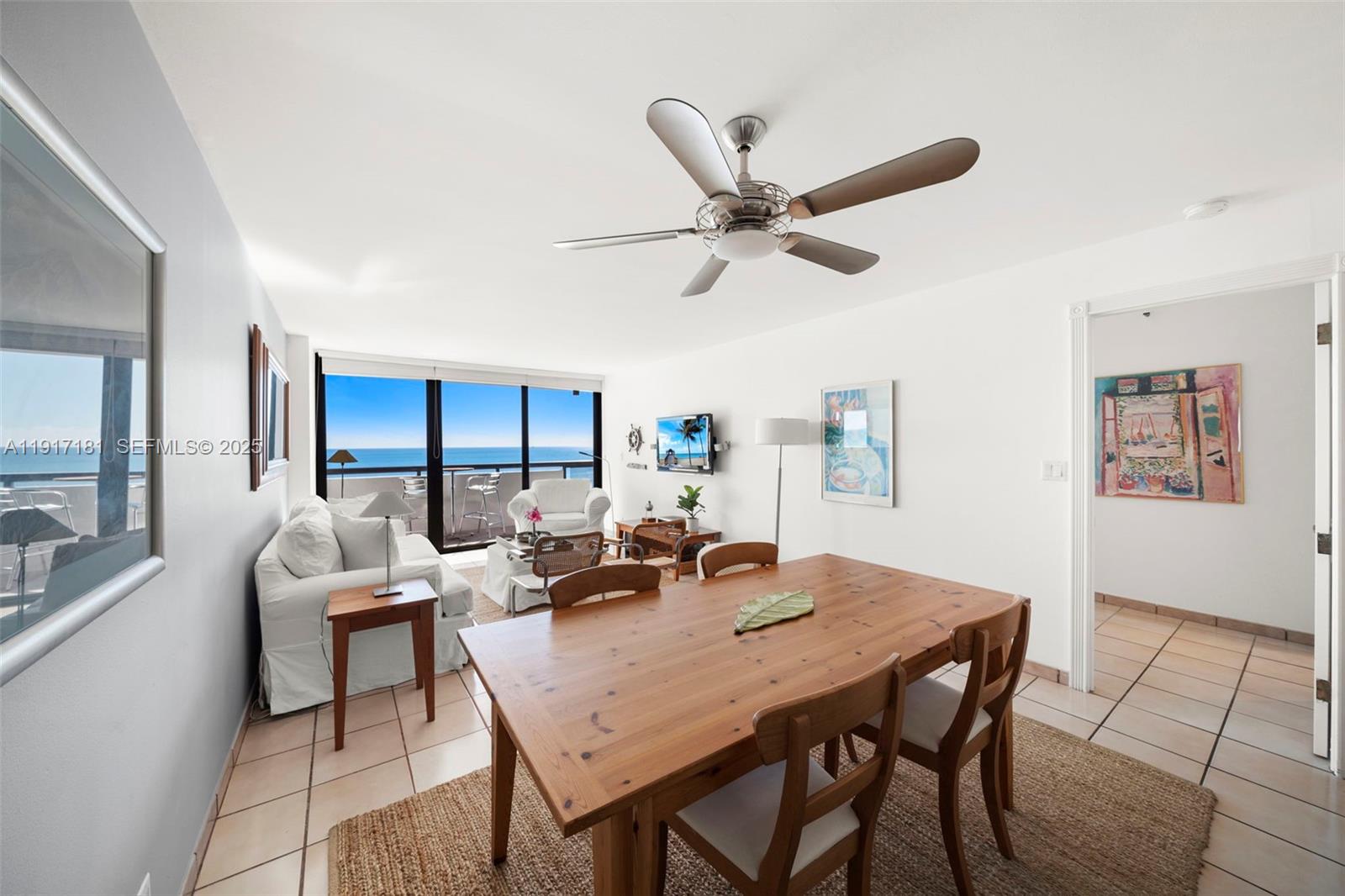 A dining and living area features a wooden table, white sofa, and ocean view balcony — 2555 Collins Ave # 805, Miami Beach FL 33140, MIAMI BEACH, FL