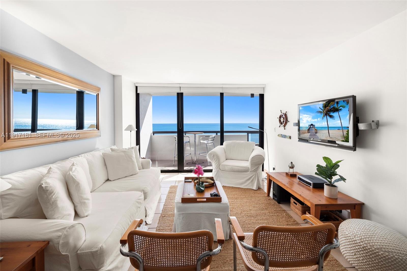 A living room with white furniture, a wooden media console, and a balcony overlooking ocean — 2555 Collins Ave # 805, Miami Beach FL 33140, MIAMI BEACH, FL