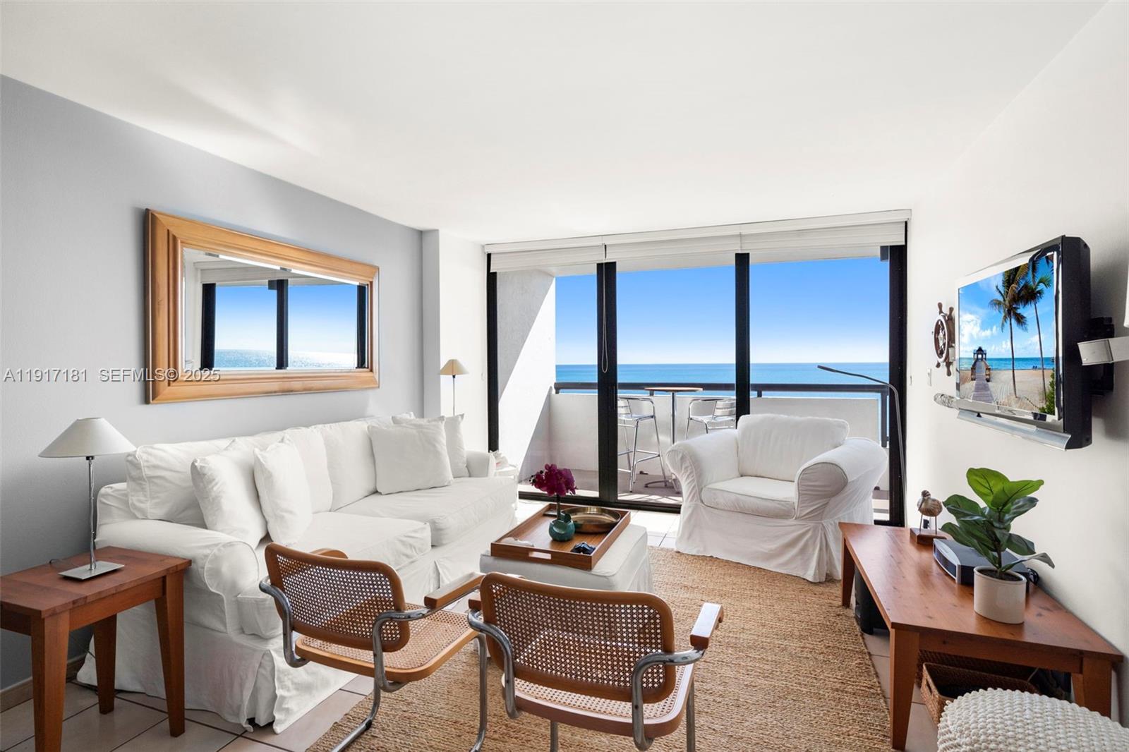 A living room with white furniture, a wooden coffee table, and a balcony overlooking ocean — 2555 Collins Ave # 805, Miami Beach FL 33140, MIAMI BEACH, FL