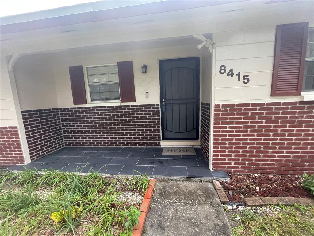 The exterior of a house features a brick facade, a front porch, and a dark door — 8415 N GOMEZ AVENUE, TAMPA, FL
