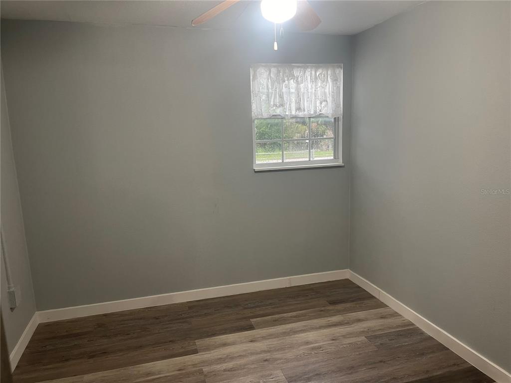 An empty bedroom features light gray walls, wood-look flooring, a ceiling fan, and a window — 8415 N GOMEZ AVENUE, TAMPA, FL