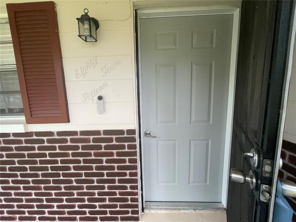 A light gray front door is set into a wall with brick siding and shutters — 8415 N GOMEZ AVENUE, TAMPA, FL