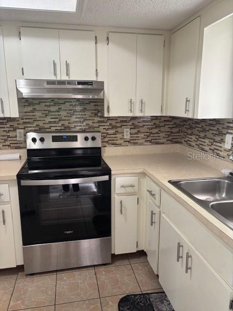 A kitchen features white cabinets, a stainless steel stove, a tiled backsplash, and light countertops — 10405 SW 98TH TERRACE, OCALA, FL