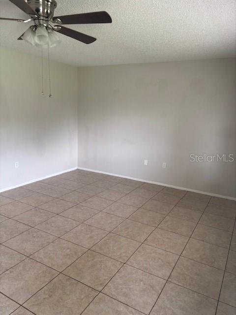 An empty room features light-colored walls, a ceiling fan, and beige tile flooring — 10405 SW 98TH TERRACE, OCALA, FL