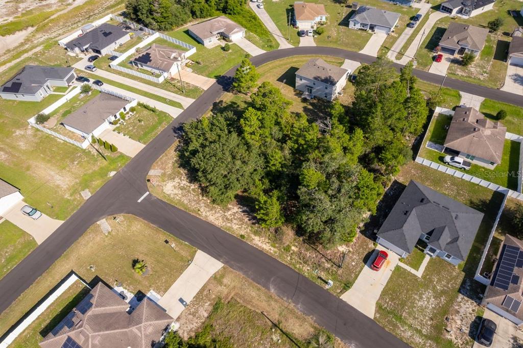 An aerial view shows a vacant, tree-covered residential lot surrounded by suburban houses and streets — 2017 MAPLE LANE, POINCIANA, FL