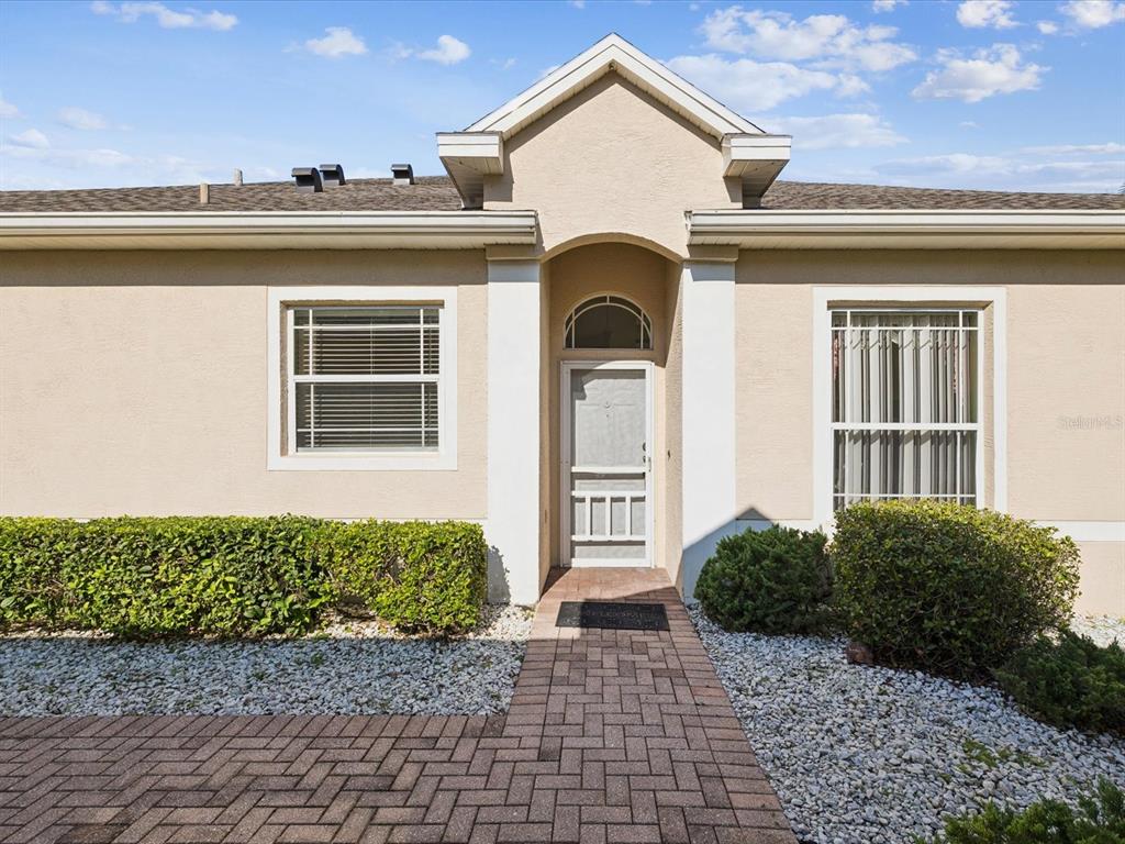 A beige house exterior features a front door with a storm door and a walkway — 2649 TOTTENHAM DRIVE, NEW PORT RICHEY, FL