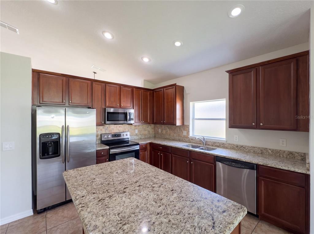 A kitchen features dark wood cabinets, granite countertops, stainless steel appliances, and a central island — 457 MARATHON LANE, SANFORD, FL