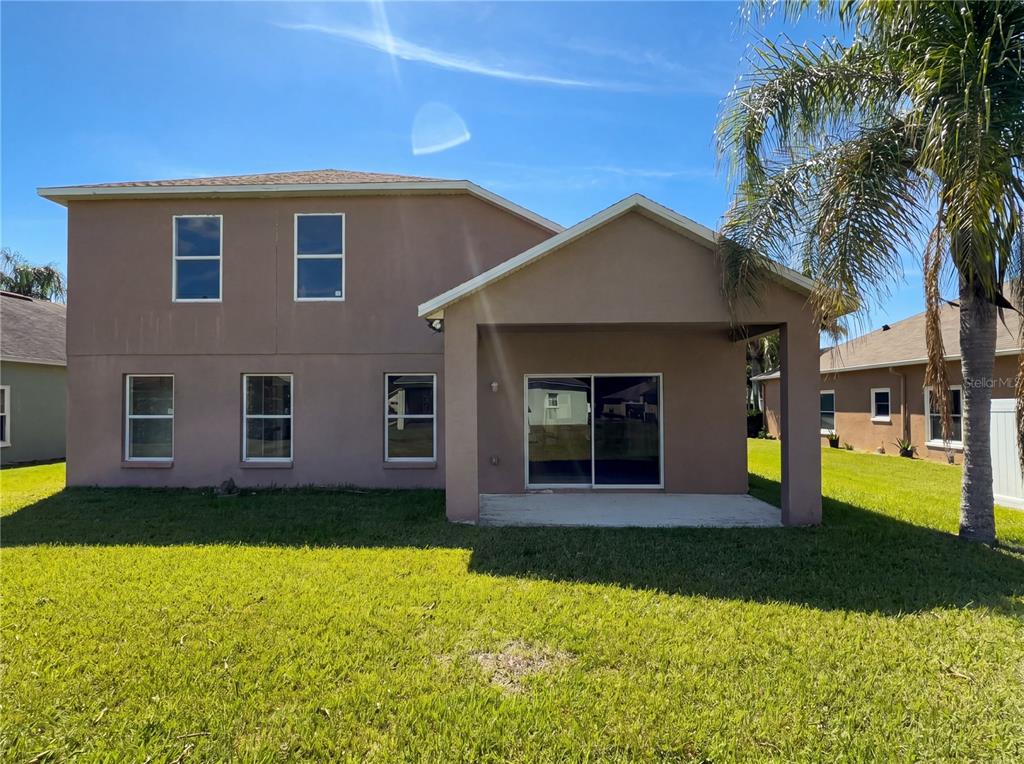 The rear exterior of a two-story tan house features a covered patio and sliding doors — 457 MARATHON LANE, SANFORD, FL