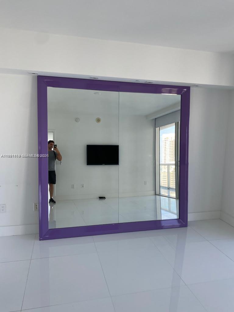 A room features a large, purple-framed mirrored wall and white tile flooring — 495 Brickell Ave # 2902, Miami FL 33131, MIAMI, FL