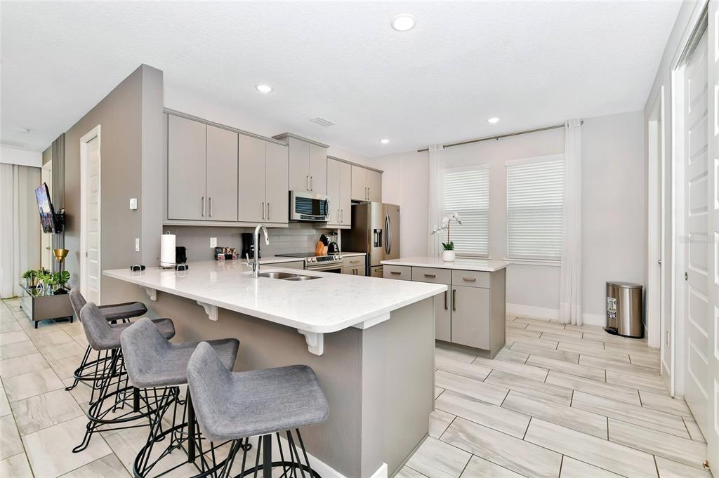 A modern kitchen features gray cabinets, white countertops, a central island, and three bar stools — 393 SOUTHFIELD STREET, KISSIMMEE, FL