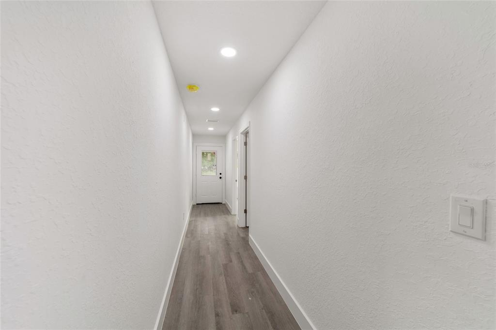 A narrow hallway with white walls, recessed lighting, and gray wood-look flooring leads to a door — 6845 SE 22ND AVENUE, OCALA, FL