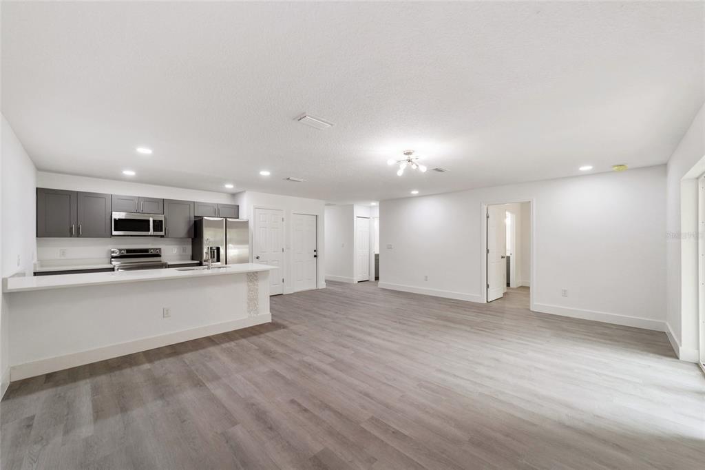 A modern open-concept kitchen and living area with gray cabinets and light wood-look flooring — 6845 SE 22ND AVENUE, OCALA, FL