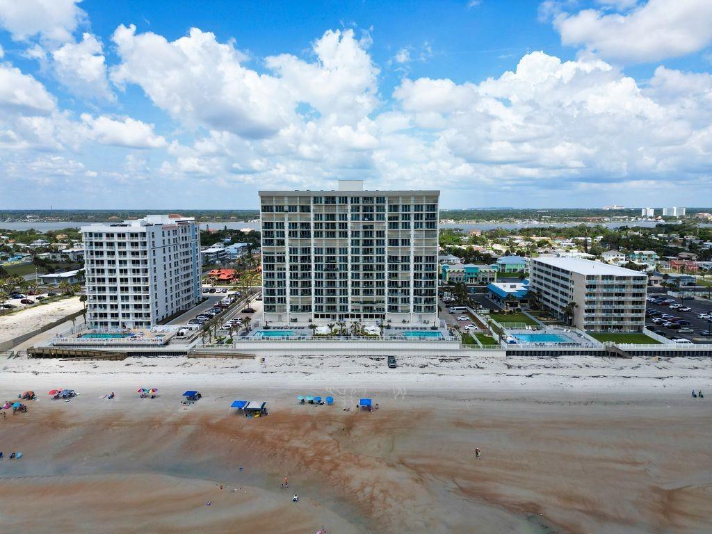 An aerial view of three beachfront condominium buildings along a sandy shoreline under a cloudy sky — 2055 S ATLANTIC AVENUE UNIT 1410, DAYTONA BEACH, FL