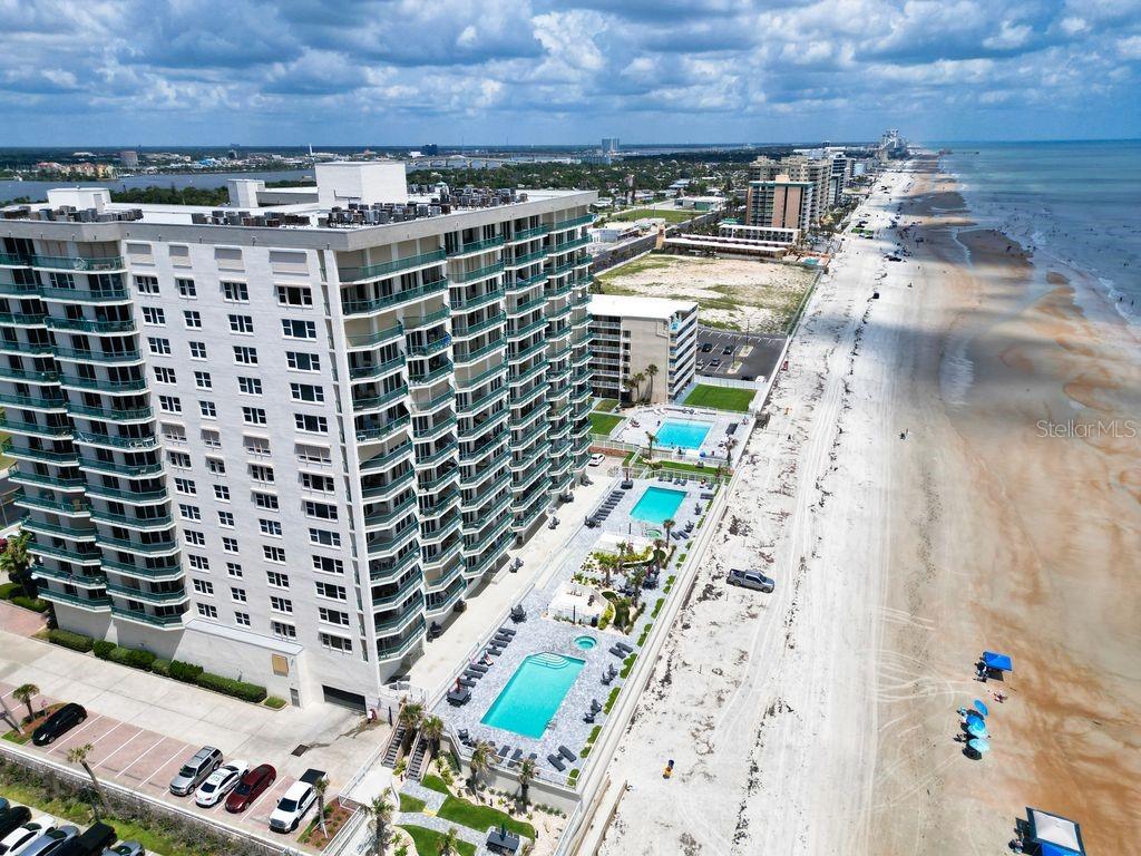 An aerial view shows a tall beachfront condominium building with multiple swimming pools and parking — 2055 S ATLANTIC AVENUE UNIT 1410, DAYTONA BEACH, FL