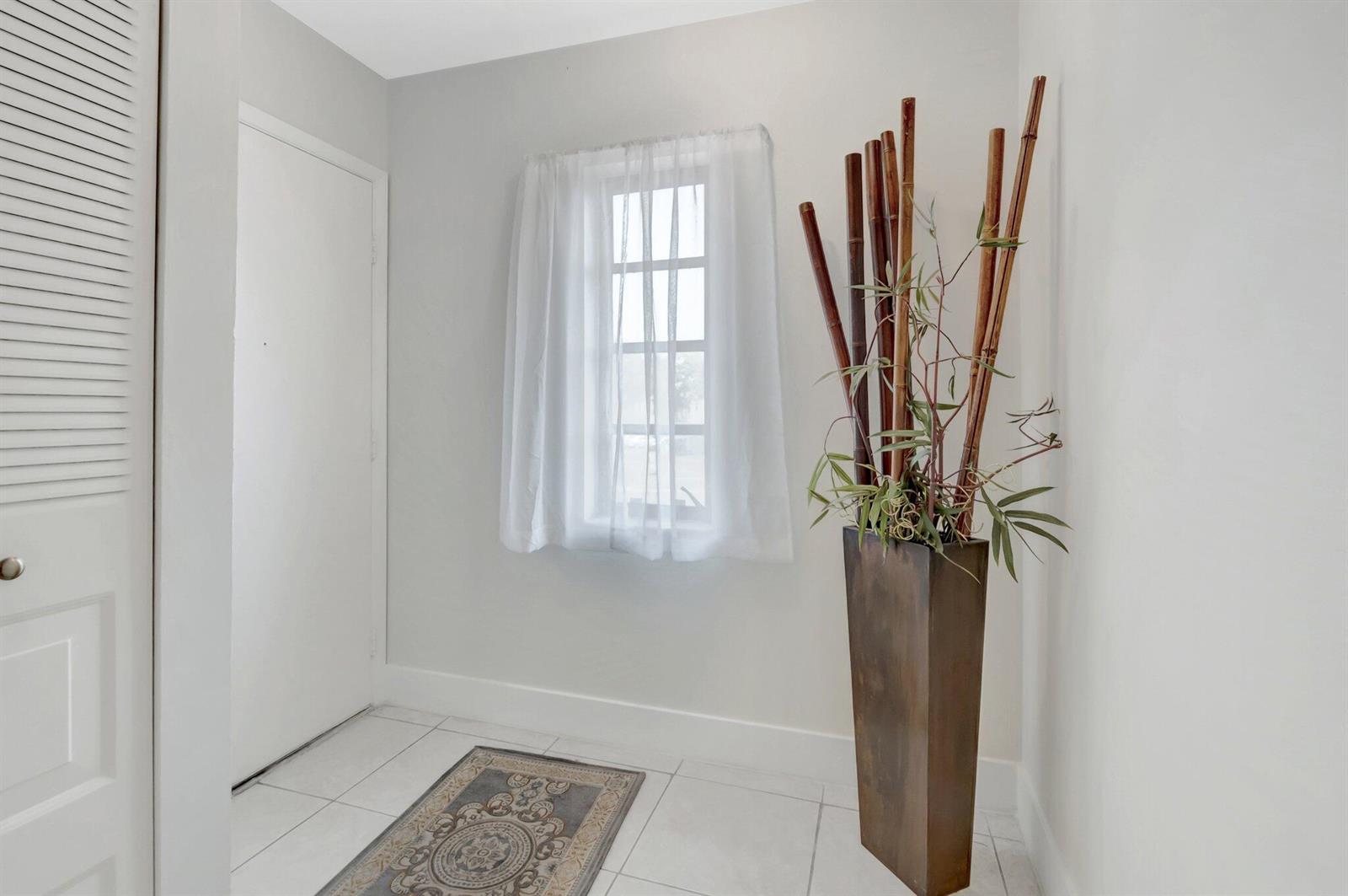 A bright entryway features white tile flooring, a window with sheer curtains, and a tall planter — 21214 Lago Circle # 8f, Boca Raton FL 33433, BOCA RATON, FL