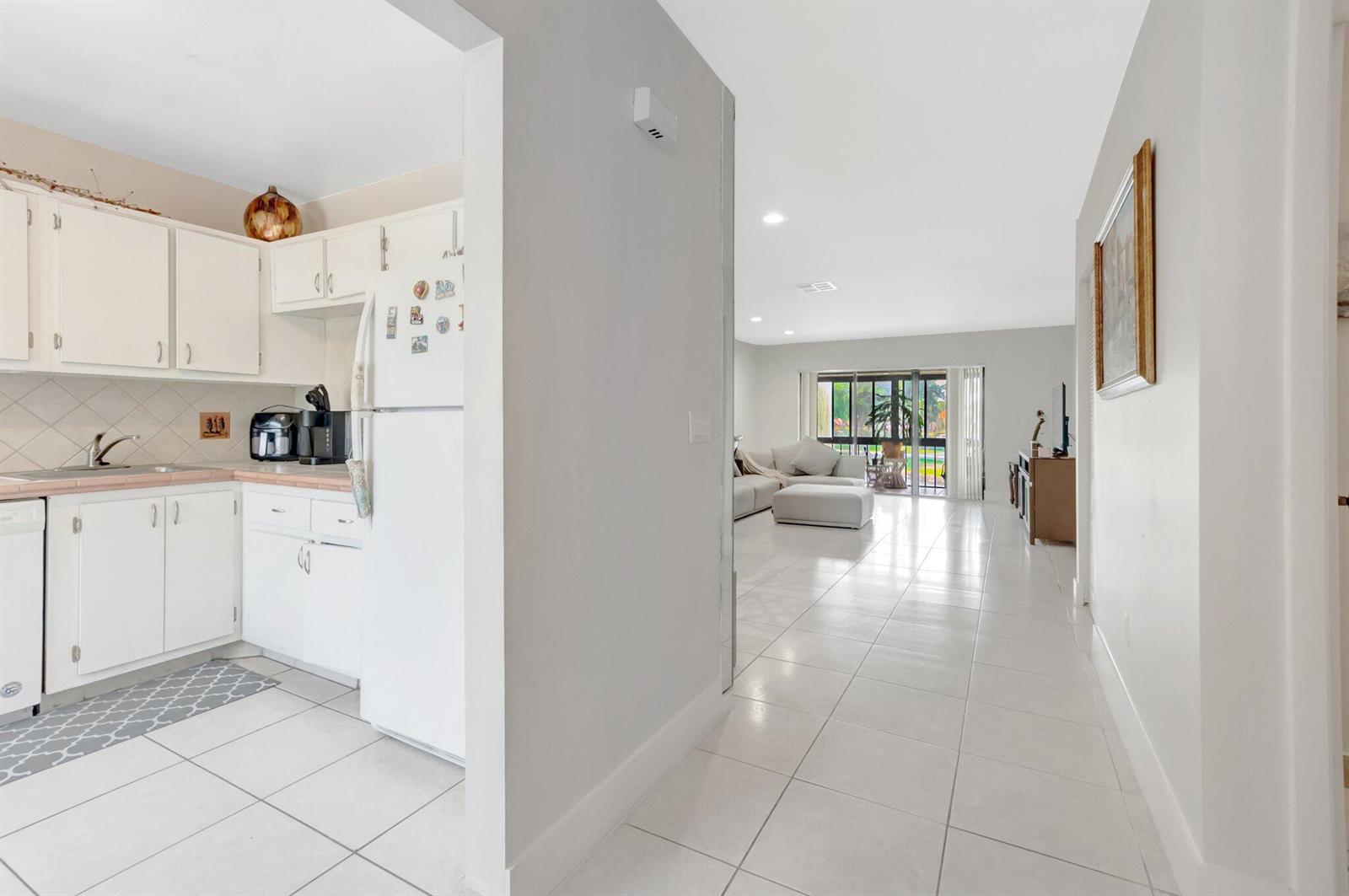 A white kitchen with tile floors opens into a bright living area with sliding doors — 21214 Lago Circle # 8f, Boca Raton FL 33433, BOCA RATON, FL