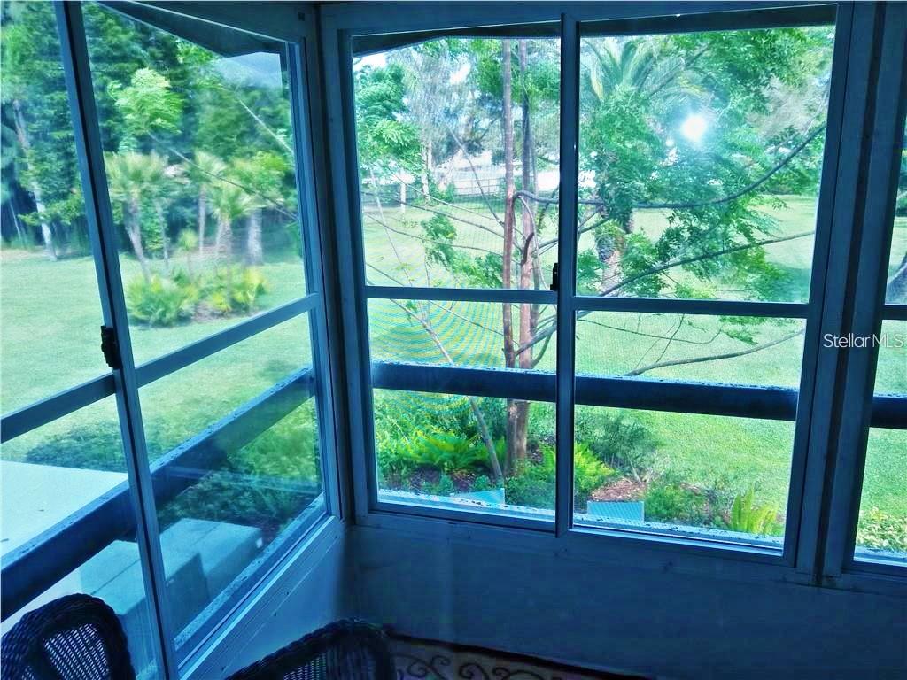 A screened-in porch overlooks a grassy backyard with trees and foliage — 2531 FLAMINGO BOULEVARD UNIT L25, BRADENTON, FL