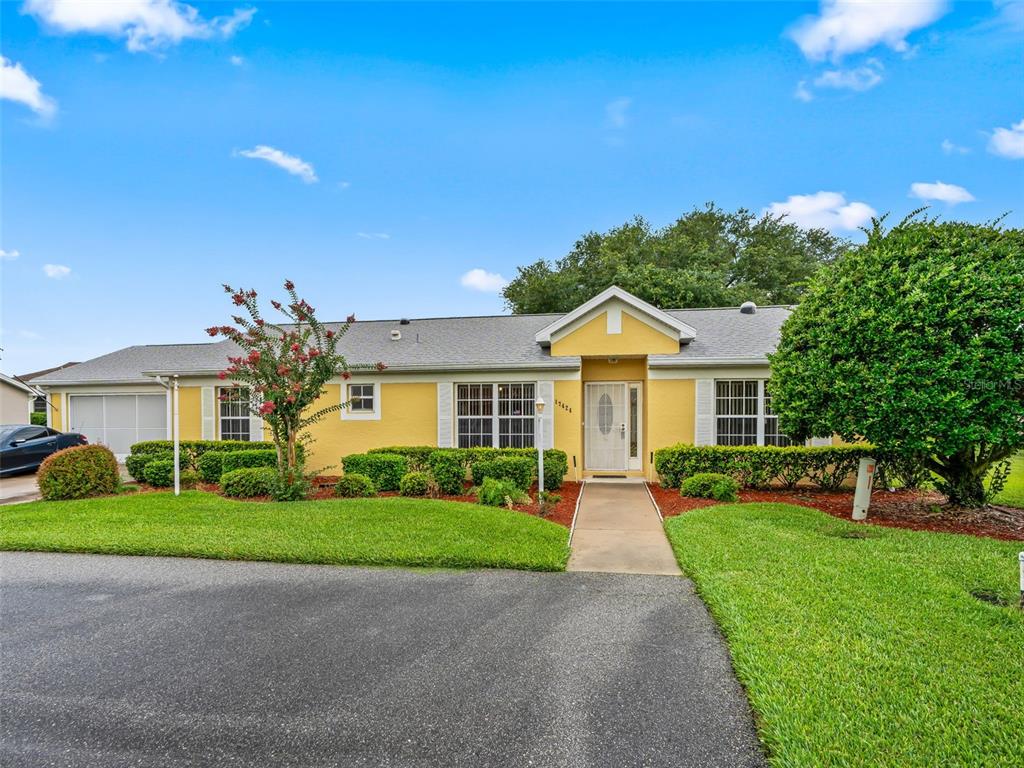 A yellow single-story house with a garage, a front walkway, and a landscaped lawn — 17424 SE 111TH AVENUE, SUMMERFIELD, FL