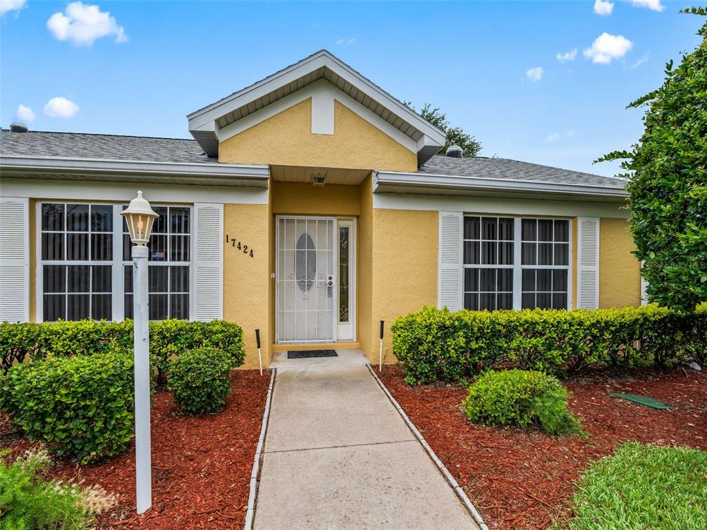 A yellow single-story house features a concrete walkway leading to a white front door — 17424 SE 111TH AVENUE, SUMMERFIELD, FL