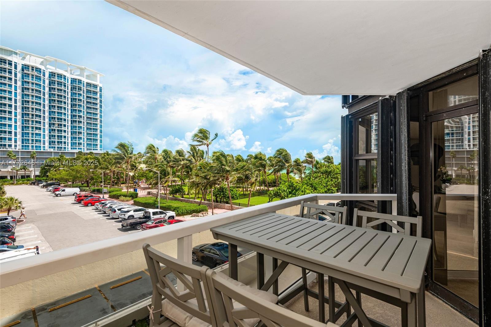 A balcony with a table and chairs overlooks a parking lot and palm trees — 6423 Collins Ave # 309, Miami Beach FL 33141, MIAMI BEACH, FL