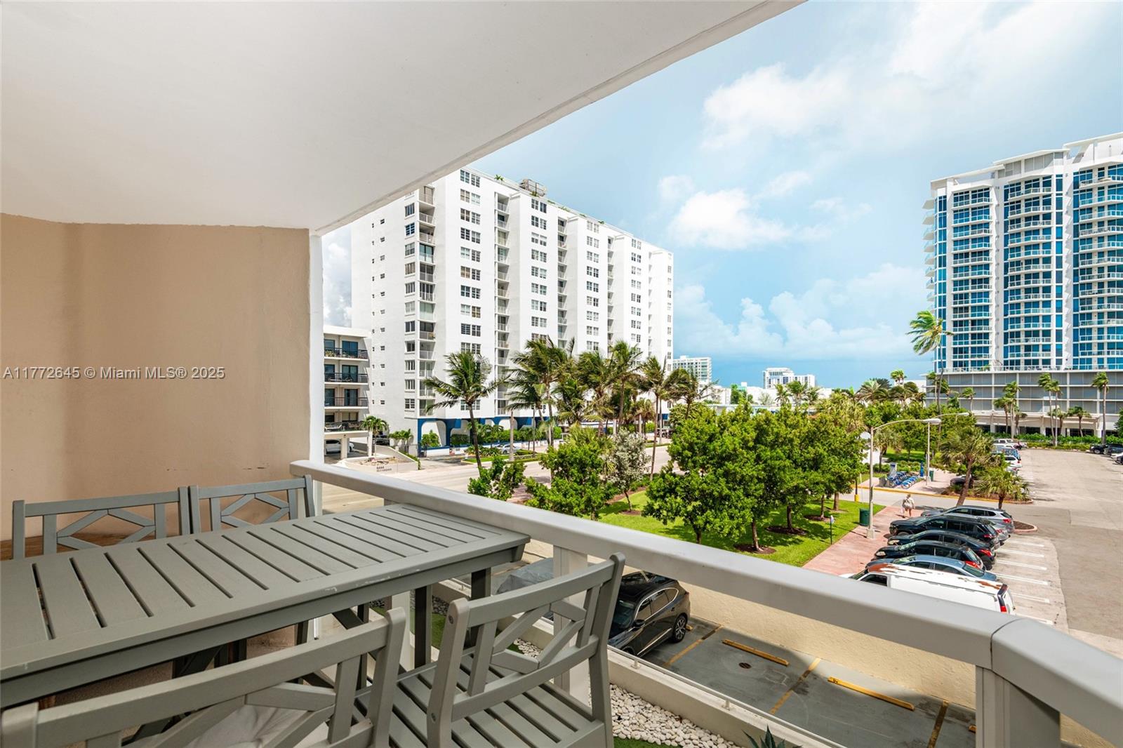 A balcony with gray furniture overlooks a parking lot, trees, and nearby high-rise buildings — 6423 Collins Ave # 309, Miami Beach FL 33141, MIAMI BEACH, FL