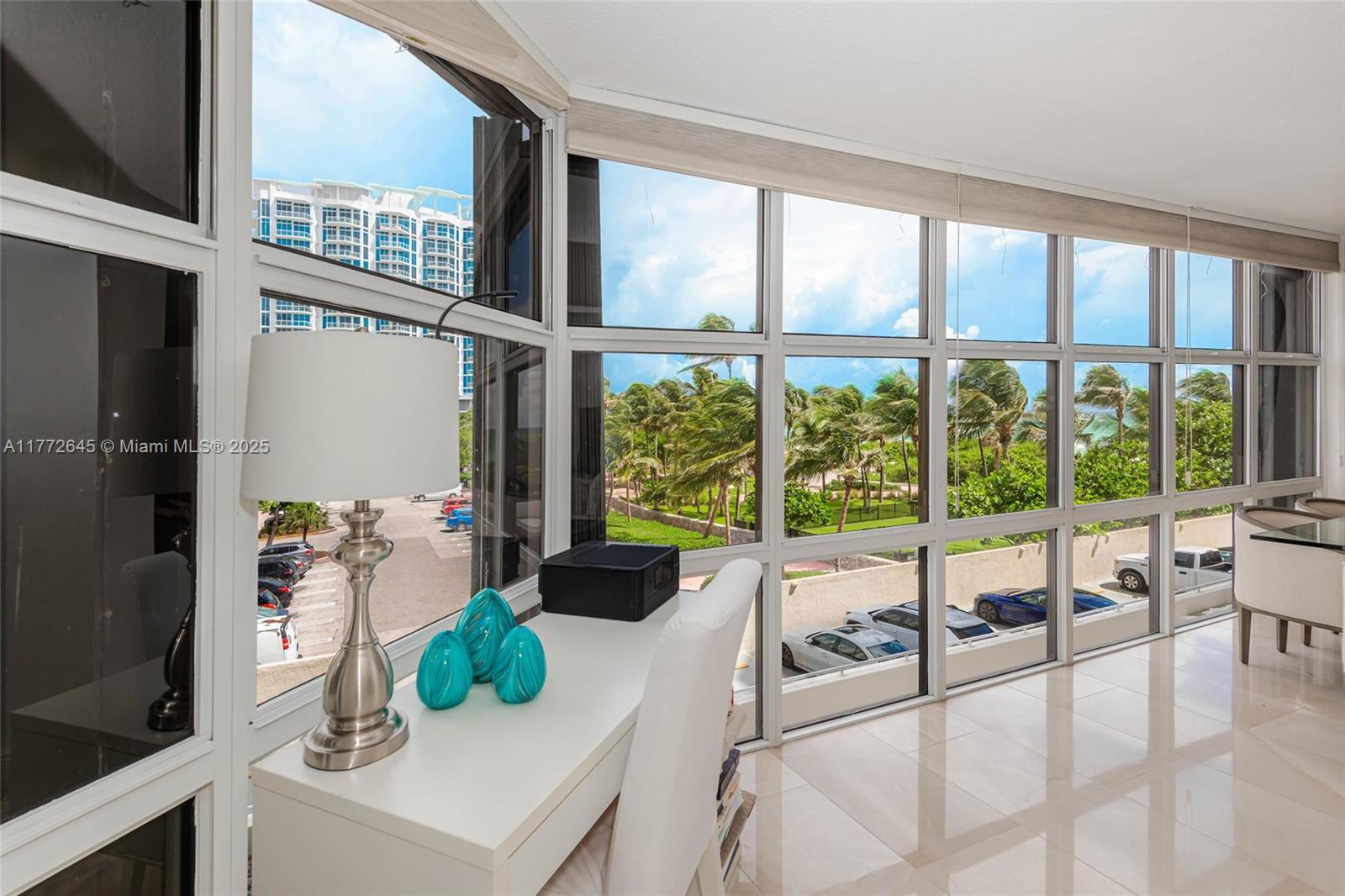 A bright room features a white desk, a lamp, and floor-to-ceiling windows overlooking a parking lot — 6423 Collins Ave # 309, Miami Beach FL 33141, MIAMI BEACH, FL