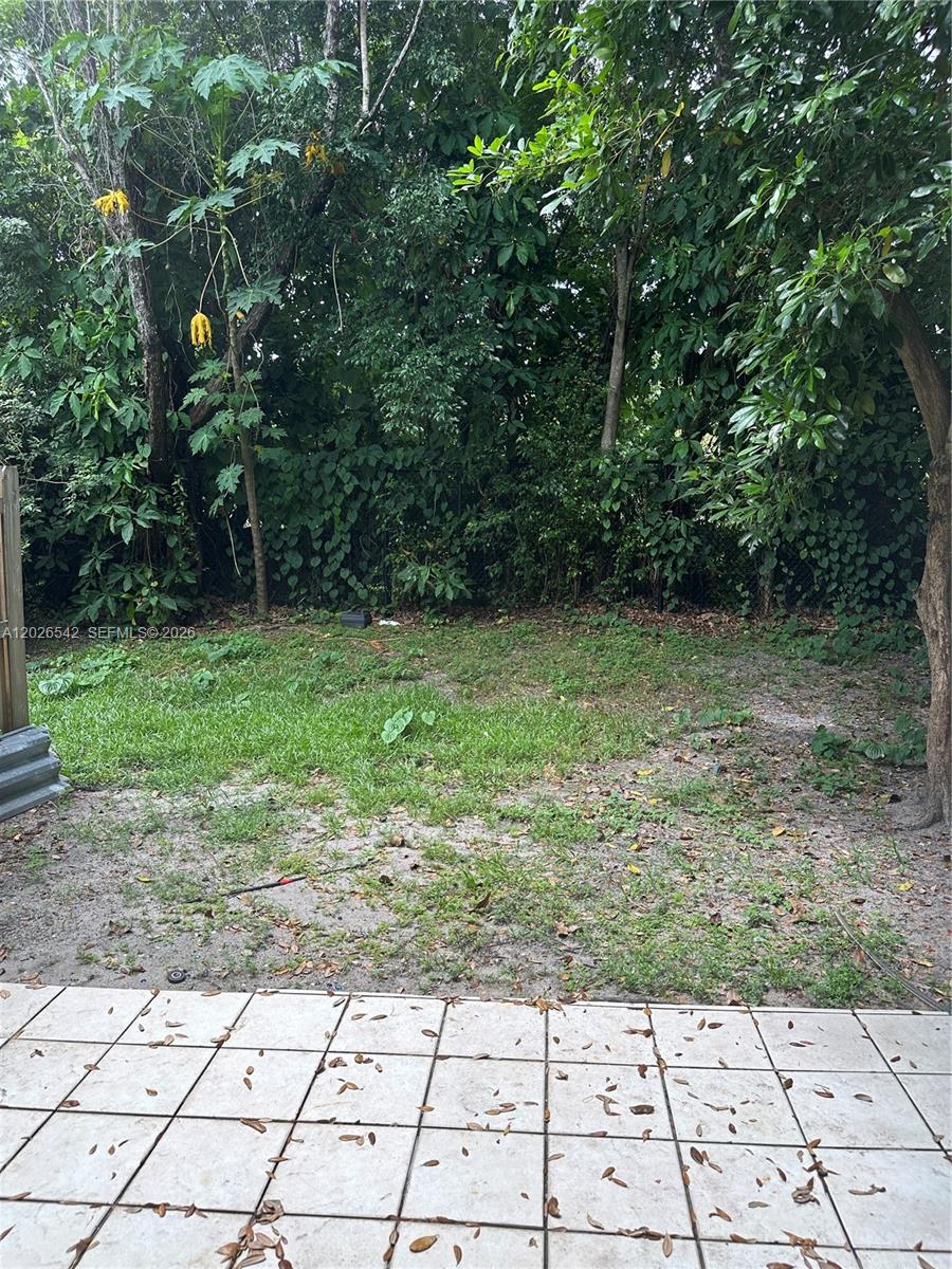 A small, partially shaded backyard features a tiled patio and dense foliage — 824 Summit Lake, West Palm Beach FL 33406, WEST PALM BEACH, FL