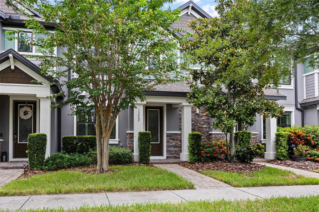 The exterior of a two-story gray townhouse features stone accents, white columns, and landscaped gardens — 13007 BATTEN LANE, ODESSA, FL