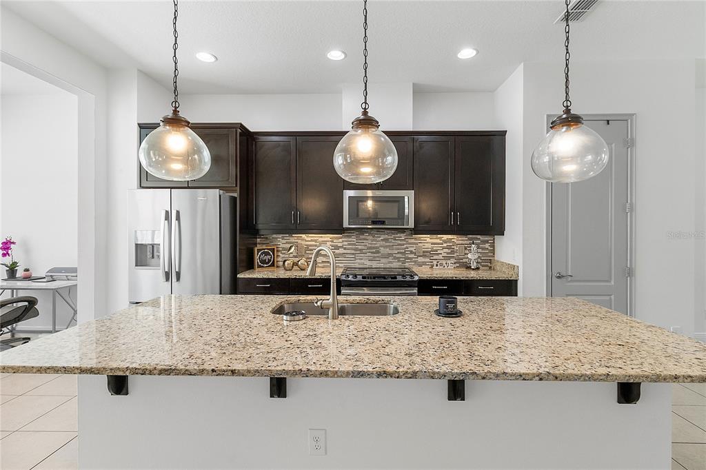 A kitchen features dark wood cabinets, granite countertops, a central island, and light tile flooring — 940 LOBELIA DRIVE, LAKE MARY, FL