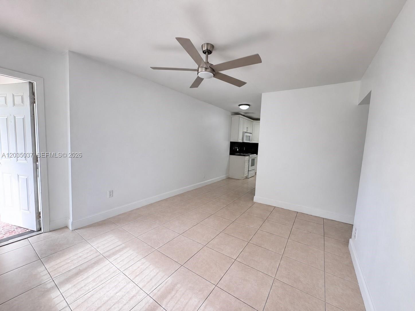 An empty room with light-colored tile flooring, a ceiling fan, and an adjacent kitchen — 1801 NE 25th Ave # 3, Pompano Beach FL 33062, POMPANO BEACH, FL