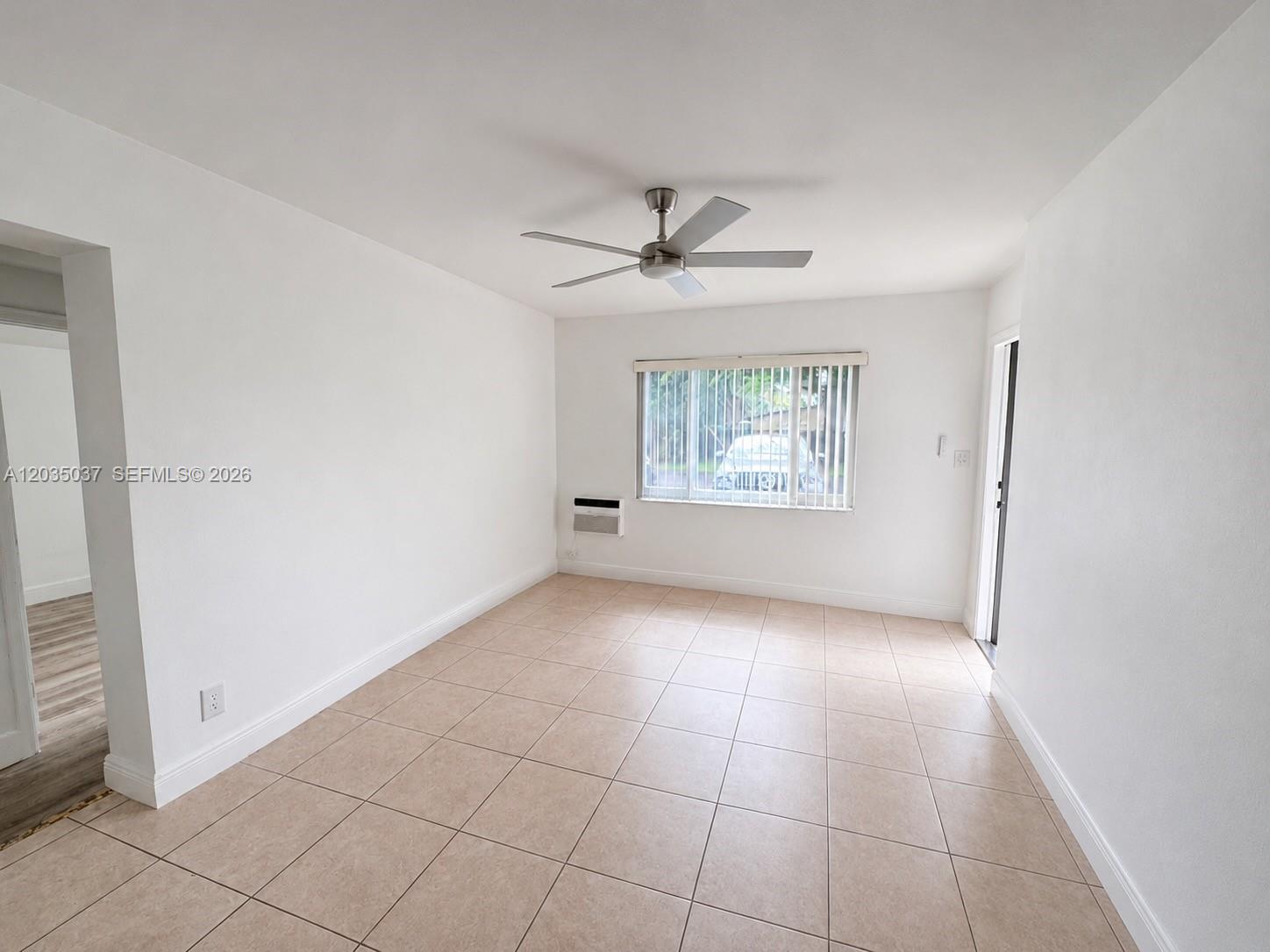 A bright, empty room features white walls, beige tile flooring, a ceiling fan, and a window — 1801 NE 25th Ave # 3, Pompano Beach FL 33062, POMPANO BEACH, FL