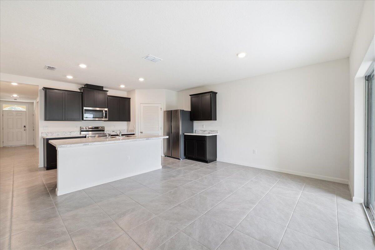 A kitchen features dark cabinets, a white island, stainless steel appliances, and light tile flooring — 1072 Roseland Road, Sebastian FL 32958, SEBASTIAN, FL