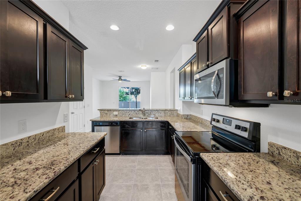 A kitchen features dark wood cabinets, granite countertops, stainless steel appliances, and tile flooring — 4824 POOLSIDE DRIVE, ST CLOUD, FL