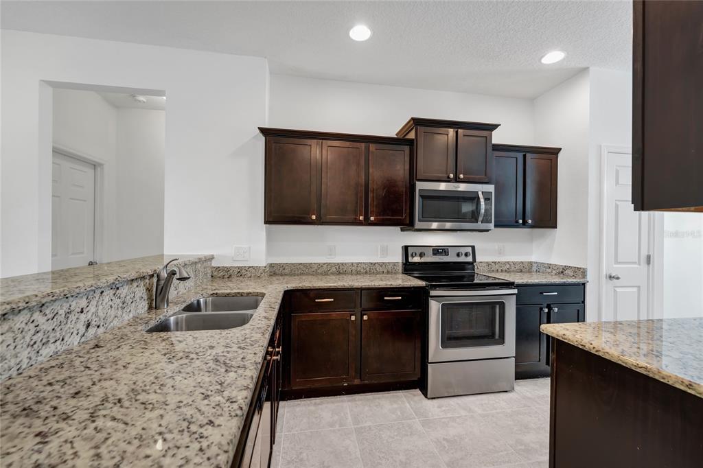 A kitchen features dark wood cabinets, granite countertops, and stainless steel appliances — 4824 POOLSIDE DRIVE, ST CLOUD, FL