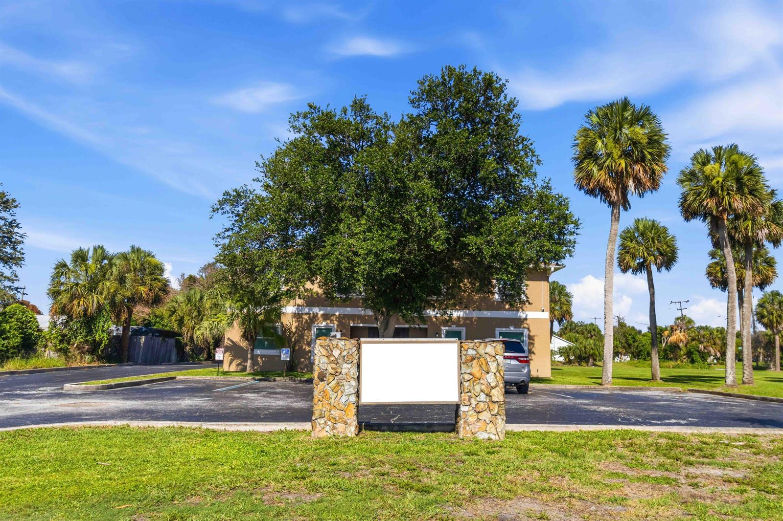 A stone-based sign stands in front of a two-story building with palm trees and parking — 111 Scott Street, Melbourne FL 32901, MELBOURNE, FL