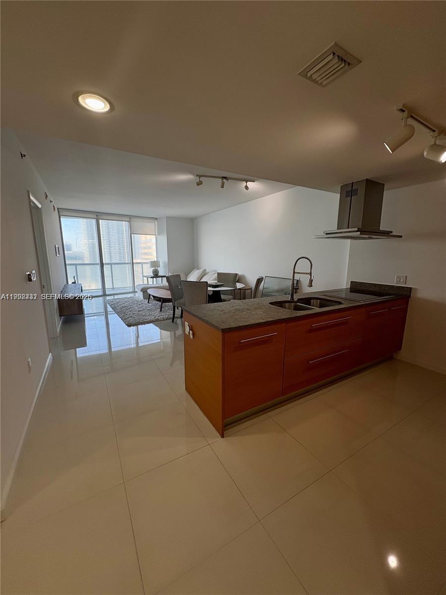 A modern kitchen with wood cabinets and a granite island overlooks a bright living area — 495 Brickell Ave # 3909, Miami FL 33131, MIAMI, FL