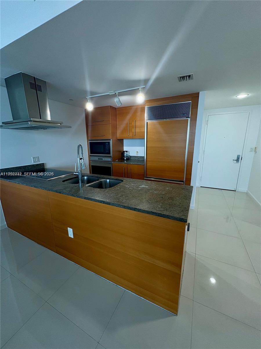 A modern kitchen features wood cabinetry, a dark stone island, and stainless steel appliances — 495 Brickell Ave # 3909, Miami FL 33131, MIAMI, FL