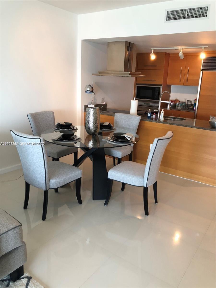 A dining area with a glass table and four chairs sits before an open kitchen — 495 Brickell Ave # 3909, Miami FL 33131, MIAMI, FL