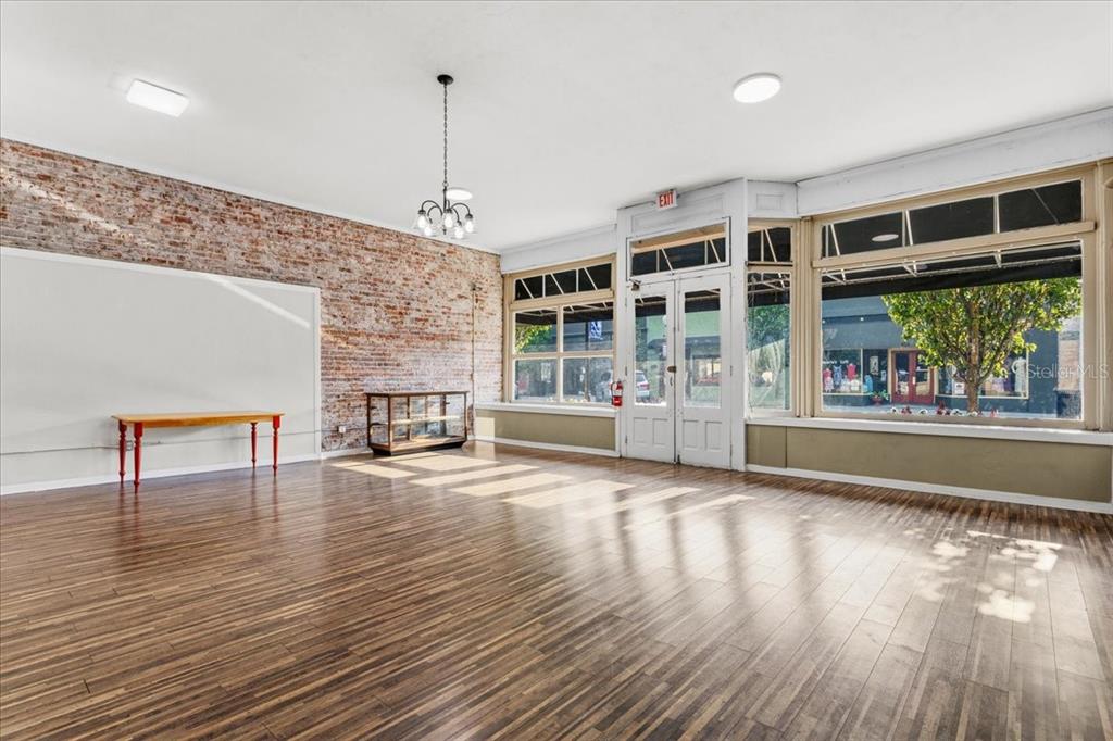 A bright commercial space features wood-look flooring, an exposed brick wall, and large storefront windows — 14827 MAIN STREET, ALACHUA, FL