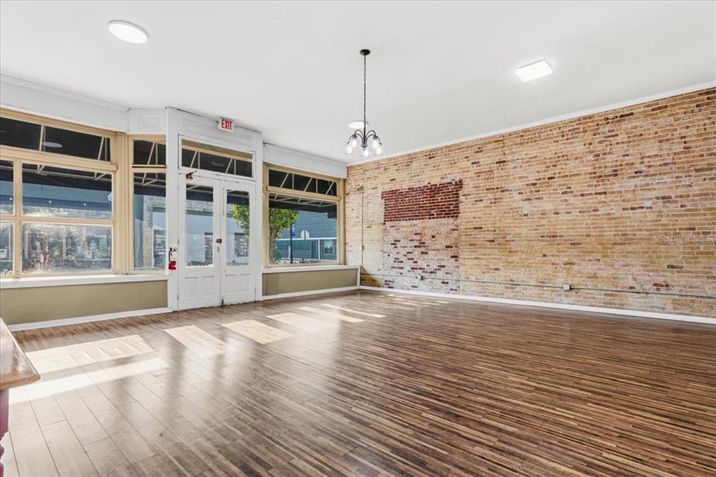 An empty commercial space features a large brick wall, wood flooring, and storefront windows — 14827 MAIN STREET, ALACHUA, FL