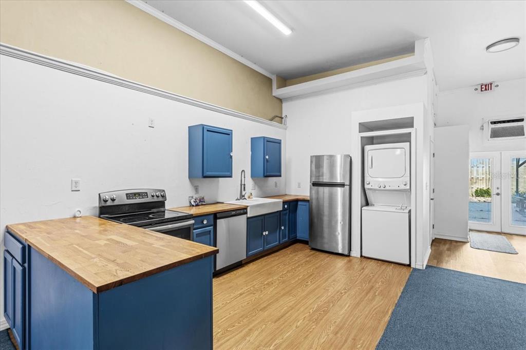 A kitchen features blue cabinets, a wooden countertop, stainless steel appliances, and a stacked laundry unit — 14827 MAIN STREET, ALACHUA, FL