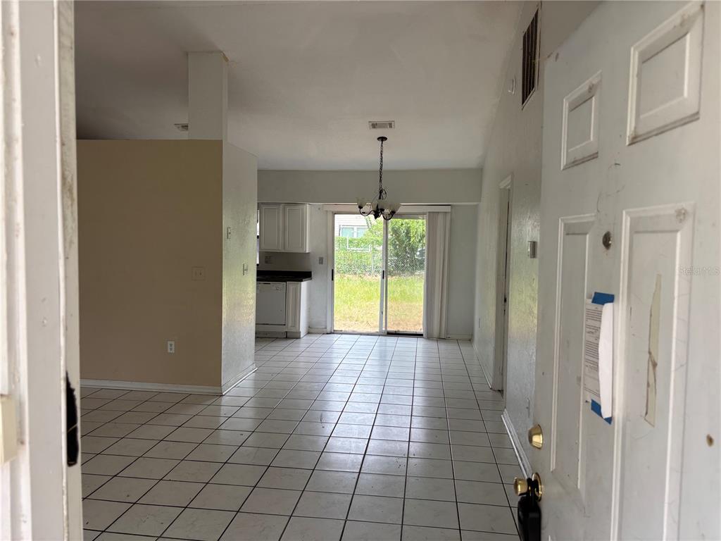 A view from an entryway into a tiled living area with a kitchen and sliding doors — 833 OGLETHORPE COURT, KISSIMMEE, FL