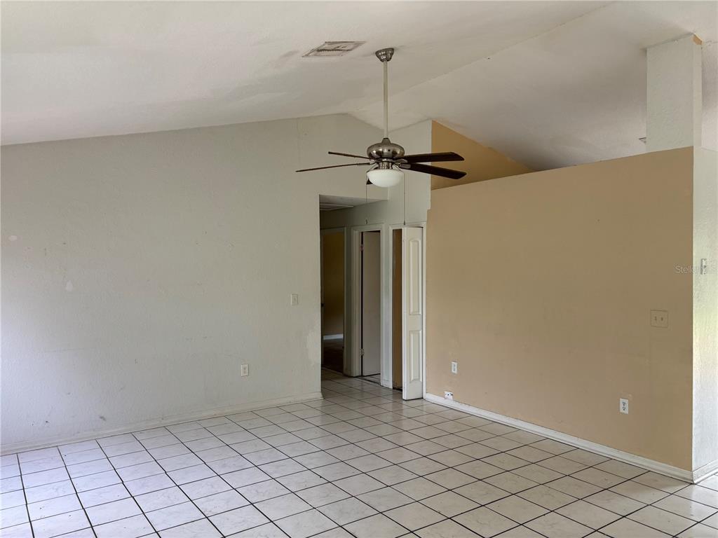 A room with white tiled floors, a vaulted ceiling, a ceiling fan, and beige walls — 833 OGLETHORPE COURT, KISSIMMEE, FL