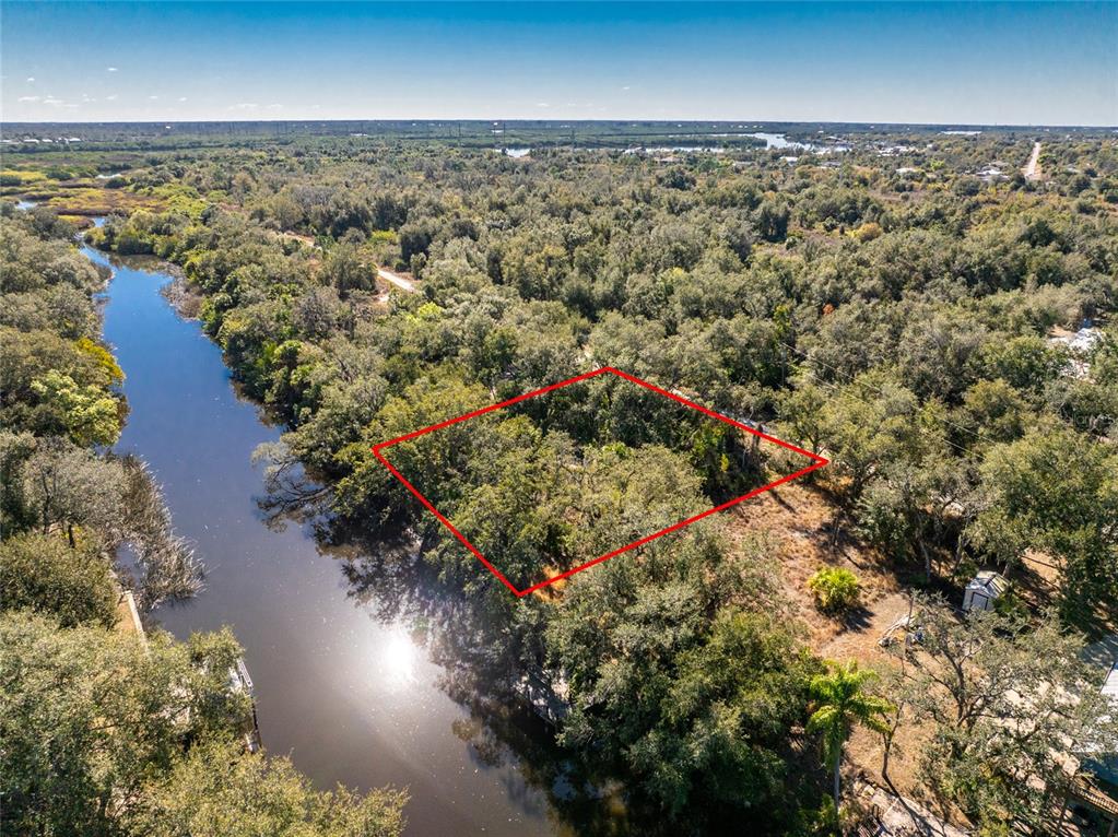 An aerial view shows a wooded waterfront lot outlined in red next to a river — 27362 SAN CARLOS DRIVE, PUNTA GORDA, FL