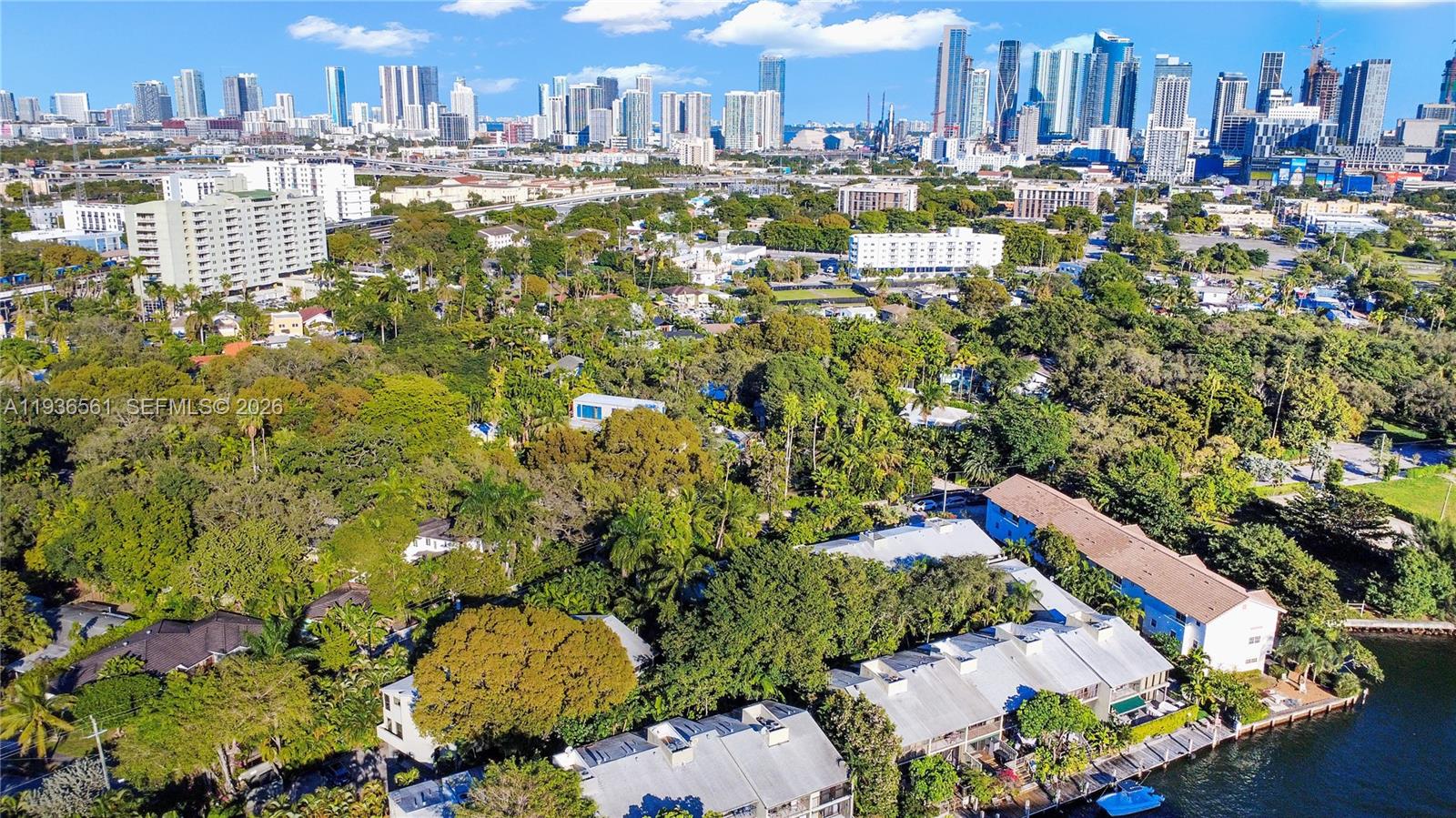 An aerial view shows a residential area with lush trees, townhouses, and a city skyline — 1000 NW N River Dr # 20, Miami FL 33136, MIAMI, FL
