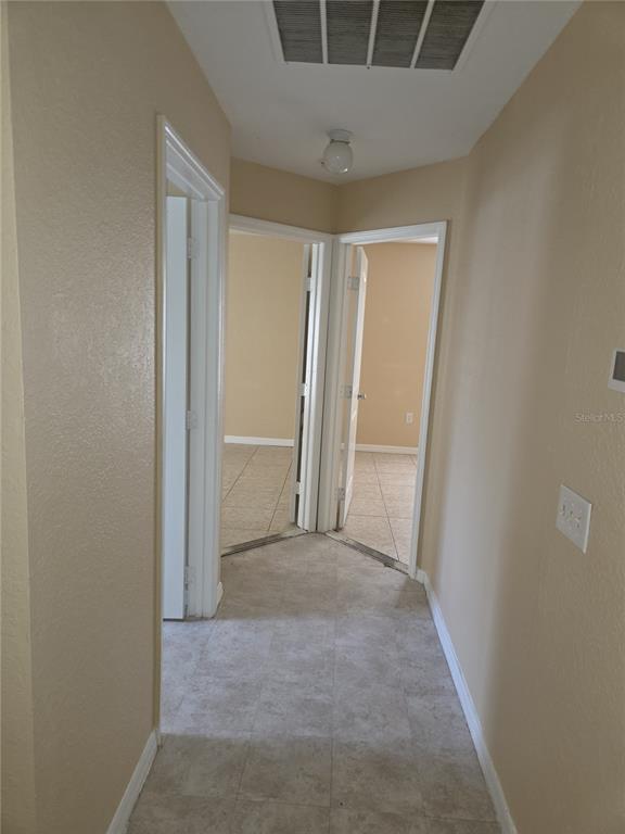 A hallway with light-colored tile flooring leads to two open doorways revealing carpeted rooms — 8 SAWFISH COURT, POINCIANA, FL