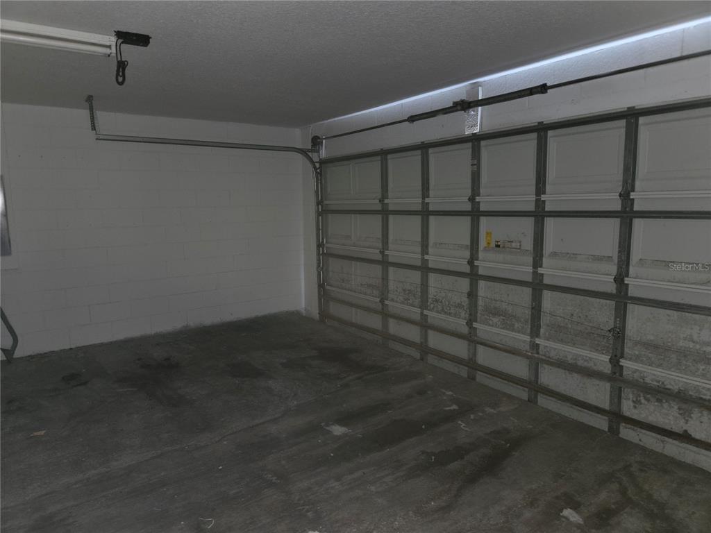 An interior view of a garage with a concrete floor and a sectional metal door — 8 SAWFISH COURT, POINCIANA, FL